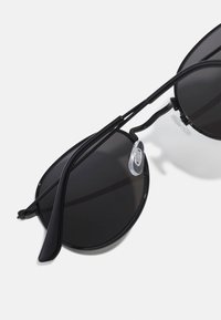 Schwarze Sonnenbrille mit runden Gläsern, dünnem schwarzen Metallrahmen und klaren Nasenpolstern. Verfügt über ein elegantes, modernes Design mit minimalen Details.
