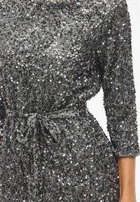 Robe en sequins gris foncé, avec une coupe ample, des manches trois-quarts et une ceinture à nouer à la taille, texturée avec des sequins circulaires.