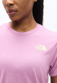 Κοντινό πλάνο ατόμου που φοράει ένα ανοιχτό μωβ t-shirt The North Face, εμφανίζοντας το γιακά και το λογότυπο στο πάνω μέρος του στήθους.