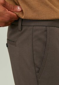 Šedé kalhoty s hladkou texturou, s boční kapsou a pasem, doplněné světle hnědým pleteným topem.