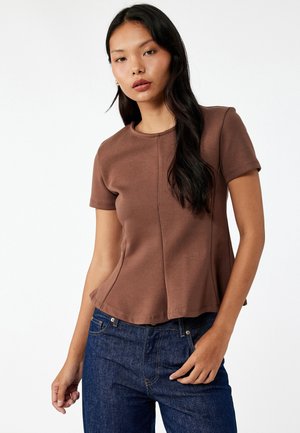 Brun kortærmet bluse med rund halsudskæring, der har en subtil udskæring nederst og en glat, blød tekstur. Bæres med mørkeblå jeans.