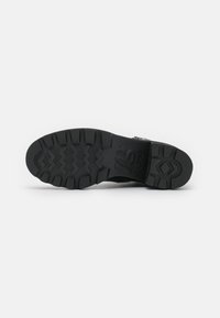Semelle de chaussure en caoutchouc noir avec un motif en zigzag, des rainures profondes et une marque. Conçue pour l'adhérence et la durabilité.