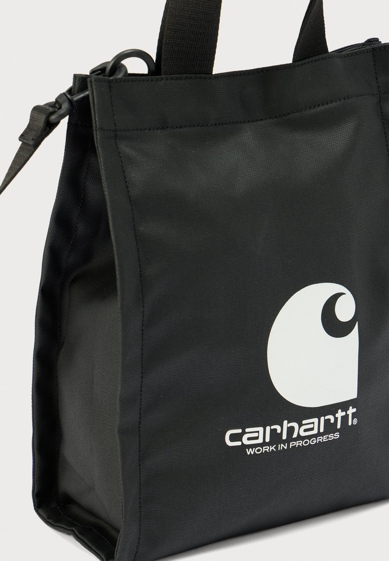 Borsa tote in nylon nero con doppi manici, caratterizzata da un logo Carhartt bianco. Il design è strutturato con cuciture visibili e una texture liscia.