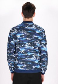 Blauwe bomberjack met een golfpatroon in verschillende tinten blauw en wit. Ribgebreide manchetten en zoom, lichtgewicht materiaal met een gladde afwerking.