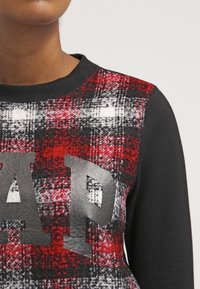 Czerwony i szary sweter w kratę, z czarnymi rękawami i fakturowanym wykończeniem. Oferuje wyraźne logo "GAP" w szarym kolorze z przodu.