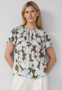 Chemisier court à manches courtes en marron avec des motifs floraux blancs et bleu clair. Présente un col froncé et une coupe décontractée.