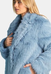 Cappotto in pelliccia sintetica di un blu chiaro con una texture spessa e soffice e un ampio colletto. Presenta maniche larghe e tasche laterali per un tocco in più.