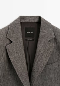 Blazer in lino marrone con texture, colletto a risvolto, taschino sul petto e etichetta interna nera con la scritta "Massimo Dutti."