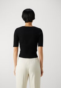 Černý krátký žebrovaný top s přiléhavým střihem, kulatým výstřihem a bezšvovým zadním dílem. Nošen s krémovými kalhotami.