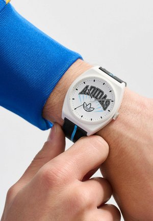 Montre analogique blanche avec le logo Adidas, bracelet texturé noir avec des accents bleus, cadran rond et indiqueurs d'heures et de minutes simples.