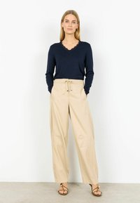 Tmavomodrý dlhý top s čipkovým lemom a béžové široké nohavice s pásom na šnúrku a detailmi vrecka vpredu. Sandále so zlatými akcentmi.