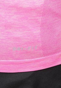 Lähikuva vaaleanpunaisesta urheilukankaasta, jossa on Dri-FIT-teksti ja verkkoventilaatiopaneelit mustan materiaalin yläpuolella.