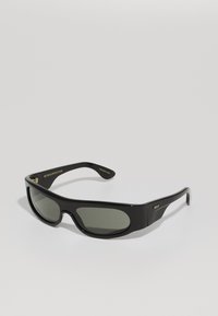 Black sunglasses with wraparound design, dark gray lenses, and glossy finish. Features gold branding on the temple and a sleek shape.