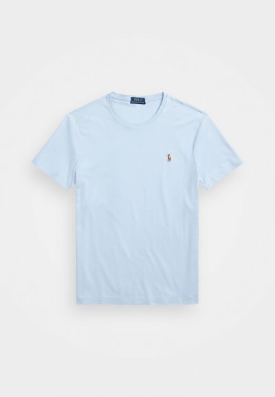 Camiseta de algodão azul claro com gola redonda e mangas curtas. Apresenta um pequeno logótipo bordado no lado esquerdo do peito. Textura suave.