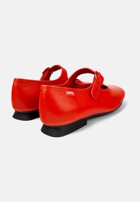 Scarpe Mary Jane in pelle rossa con punta rotonda e suola in gomma nera piatta. Presentano una cinghia laterale con una fibbia decorativa e dettagli intagliati.