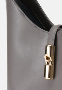 Γκρι δερμάτινη τσάντα χειρός με λεία υφή, που διαθέτει κλείσιμο με μεταλλικό κούμπωμα σε χρυσό τόνο και κομψό σχεδιασμό.