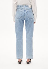 Vaqueros de tiro alto de color azul claro con perneras rectas, que cuentan con dos bolsillos traseros y una etiqueta de marca en la cintura, combinados con zapatos negros de punta abierta.
