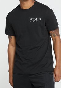 Černé bavlněné tričko s vyšívaným textem "CROSSFIT" a "CV FM HI" v kontrastní barvě. Krátké rukávy, kulatý výstřih, standardní střih.