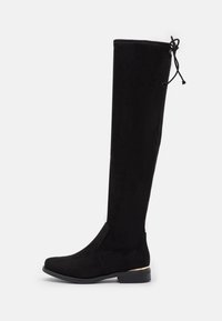 Bottes noires en daim montant jusqu'au genou, avec une texture lisse, une coupe ajustée, un dos élastique et un accent doré au talon. Semelle en caoutchouc antidérapante.