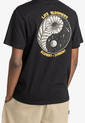 Czarna bawełniana koszulka z dużą białą i żółtą grafiką stokrotki w otoczeniu elementów kosmicznych oraz napisem "LATE BLOOMERS ELEMENT & TIMBER!"