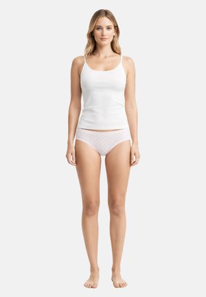 Woman standing barefoot wearing a white camisole and white hipster underwear with small pink heart patterns on a light gray background.