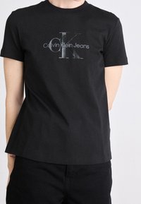 Czarna bawełniana koszulka z okrągłym dekoltem, z logo w kolorze srebrnym i napisem "Calvin Klein Jeans". Krótkie rękawy i luźny krój.