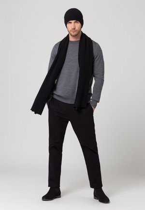 Pull gris, écharpe en tricot noire et pantalon noir. Un bonnet noir et des bottines à cheville complètent le look. Matériaux simples et texturés.
