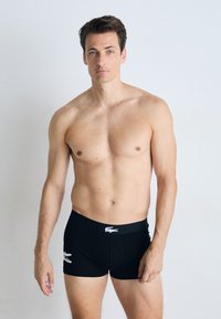 Zwarte boxershorts met een contrasterend wit logo op de tailleband, met een aansluitende pasvorm en een zachte stof. Het model staat rechtop met ontspannen armen.