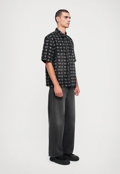 Black short-sleeve shirt with gray leaf patterns, paired with wide-leg faded black jeans and black sneakers. Minimalist design, casual fit.