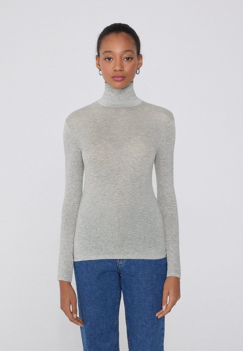 Jasnoszary sweter z golfem i długimi rękawami, wykonany z miękkiego, prążkowanego materiału. Noszony z niebieskimi dżinsami, o dopasowanym kroju.