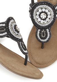 Sandali neri con perline, dotati di embellishments argentati e trasparenti, caratterizzati da un design con strappo tra le dita e una soletta imbottita in finta pelle scamosciata beige.