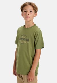 Olivově zelené bavlněné tričko s krátkým rukávem, kulatým výstřihem a předním potiskem s nápisem "Quiksilver" v tmavě modré a béžové barvě.