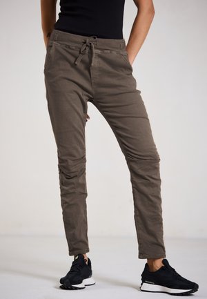 Leichte, locker sitzende olivgrüne Hosen mit elastischem Bund, Seitentaschen und strukturiertem Stoff, kombiniert mit schwarzen Sneakers.