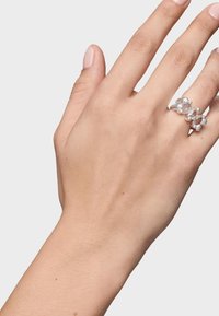 Anillo en tono plateado que presenta un grupo de cuentas redondas y facetadas, con un acento de cristal transparente, llevado en una mano con esmalte de uñas en tonos neutros.
