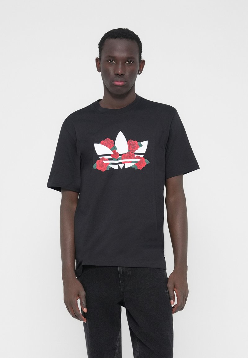 Fekete pamut póló, nagy fehér Adidas logóval és piros rózsákkal díszítve. Laza szabású, rövid ujjú és kerek nyakkivágású.