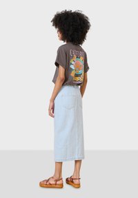 Camiseta gráfica de corte holgado en color marrón con un vibrante estampado de California. Combinada con una falda midi de mezclilla clara y sandalias marrones de tiras.