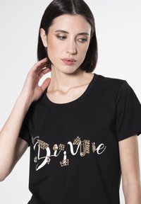 Camiseta de algodón negra con texto en blanco y piedras brillantes en tonos dorados y claros en la parte frontal, mangas cortas, escote redondo.