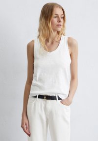 Débardeur blanc sans manches avec un design en V, fabriqué en tissu léger. Porter avec un jean blanc taille haute et une ceinture noire.