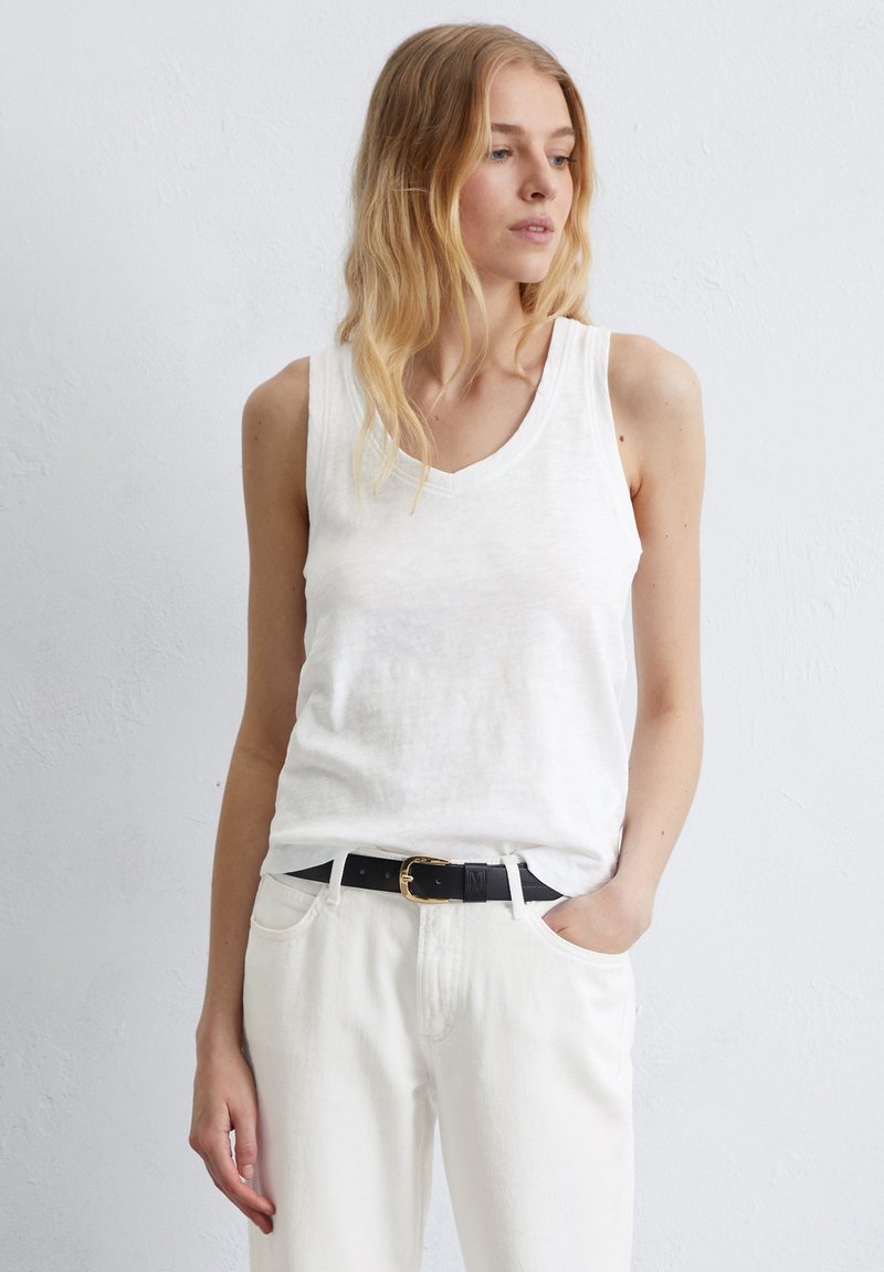 Débardeur blanc sans manches avec un design en V, fabriqué en tissu léger. Porter avec un jean blanc taille haute et une ceinture noire.