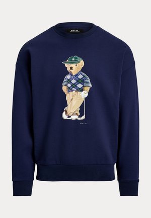 Tumesinine dressipluus, millel on karu multikas golfiriietuses, kandmas argyle-mustriga vestit ja klassikalisi pükse. Soonilised mansetid ja alläär.