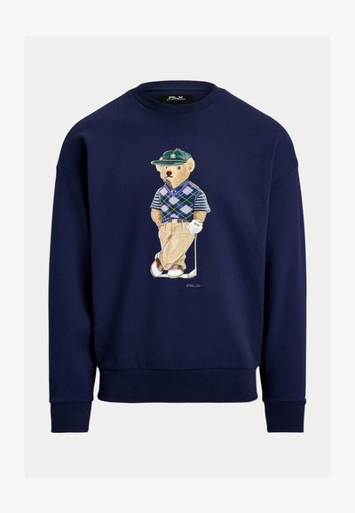 Φούτερ σε ναυτικό μπλε χρώμα με σχεδιασμό αρκούδας καρτούν ντυμένης με γκολφ, φορώντας πουλόβερ με αργκολέ μοτίβο και κλασικό παντελόνι. Με ribbed μανσέτες και τελείωμα.