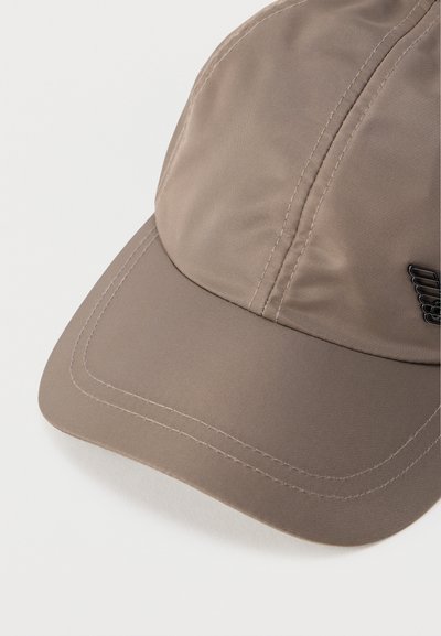 Μπεζ καπέλο του μπέιζμπολ με ραφές και μικρό μαύρο έμβλημα φτερού στην πλευρά, τοποθετημένο σε απλό λευκό φόντο.
