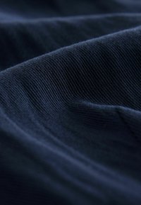 Tummansininen puuvillakangas, jolla on pehmeä, teksturoitu pinta, ja siinä on hienovaraista uritusta sekä sileitä taitteita.