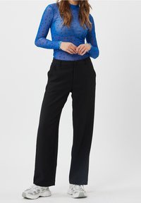 Sininen läpikuultava pitkähihaisessa paita, jossa on sydänkuvioita, yhdistettynä korkeavyötäröisiin mustiin leveälahkeisiin housuihin. Mallilla on päällään valkoiset urheilukengät.