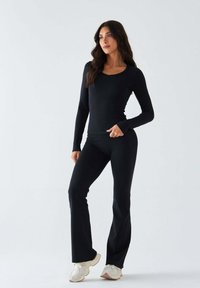 Schwarzes Langarmshirt und eng anliegende Hosen aus dehnbarem Material, mit U-Ausschnitt und ausgestellten Hosenbeinen, kombiniert mit hellen Sneakers.