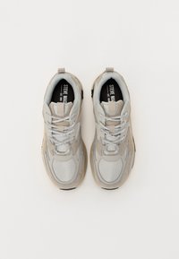 Jasnoszary sneaker z siateczkowym i zamszowym wykończeniem, grubą podeszwą, zaokrąglonym kształtem, odblaskowymi sznurówkami i logo na języku.