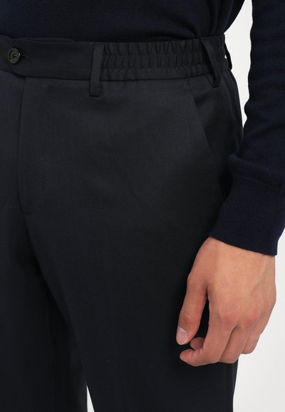 Black tailored pants with an elastic waistband, a flat front, side pockets, and a smooth, textured fabric. Double-button closure detail.