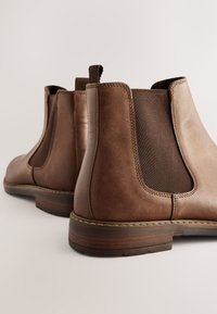 Bottes chevilles en cuir marron avec panneaux latéraux élastiques, bout rond et finition texturée. Caractérisées par un petit talon empilé et des détails de couture.