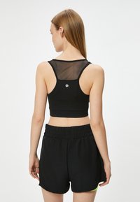 Sort sport BH med mesh rygindsats og logodetalje, parret med sorte drawstring shorts. Stoffet ser strækbart og letvægtigt ud.