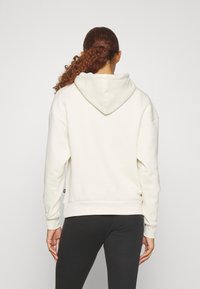 Krämfärgad, oversized hoodie med en bred huva och ribbade manschetter, parat med svarta leggings. Slät textur, minimal detaljering.